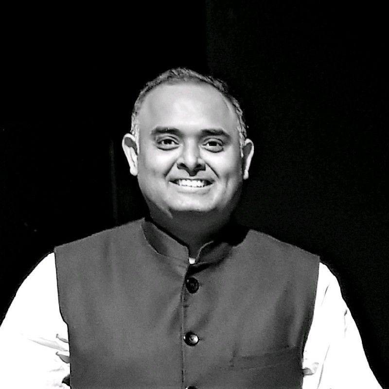 Man wearing a Nehru jacket, collared shirt, and standing against a dark background.